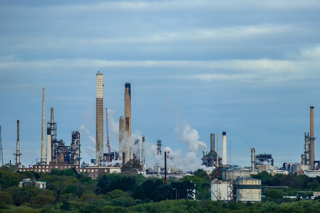Aerial view of a refinery with smokestacks and oil tanks under a cloudy sky