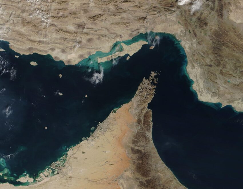 The narrow Strait of Hormuz lies between the Persian Gulf and the Gulf of Oman, separating Iran (north) from the Arabian Peninsula (south). Only about 21 miles (34 km) wide at the narrowest point and roughly 96 miles (155 km) long, about thirty percent of the world’s seaborne oil and nearly one-quarter of the liquified natural gas (LNG) supply passes through this strait — all on shipping lanes that measure only two-mile wide. It has been estimated that 21 million barrels of oil, with a value of 1.2 billion US dollars (USD), pass through the strait every day. On December 2, 2020, the Moderate Resolution Imaging Spectroradiometer (MODIS) on board NASA’s Terra satellite acquired a true-color image of the Strait of Hormuz. The arid landscape of Iran sits in the north, with Qeshm Island, the largest in the Persian Gulf, just off the Iranian coast. The tiny Strait of Khuran separates the island and the mainland and bounds a wetland of international importance, recognized by Ramsar. These wetlands provide critical habitat to two globally threatened species: the Dalmatian Pelican and the Green sea turtle. In the south, the rocky and rugged Musandam Peninsula juts into the Strait of Hormuz. The tip of the peninsula is filled by the Musandam Governate, an exclave of Oman. To the south, the land on the peninsula belongs to the United Arab Emirates.