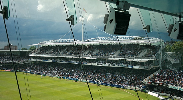 The Grand Stand from the Media Centre, Lord's Cricket Ground Looking out through the thick plate glass of the Lord's media centre towards the Grand Stand. There was heavy cloud - as well as moments of sunshine. The photograph looks as though there is a floodlight beyond the stand, but it is an illusion; an MCC flag flutters in the breeze.