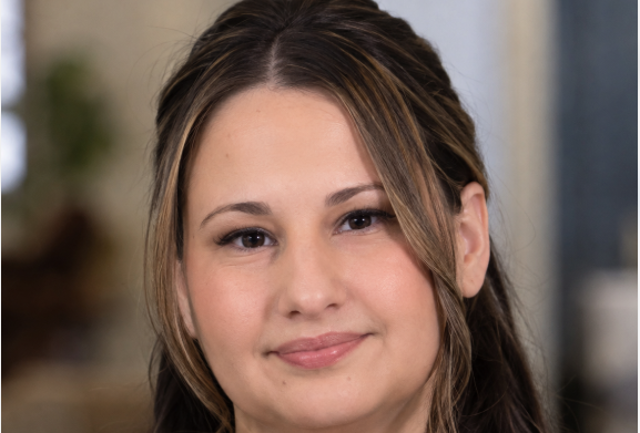 Portrait of Gypsy Rose Blanchard with long brown hair and a slight smile against a softly blurred indoor background.